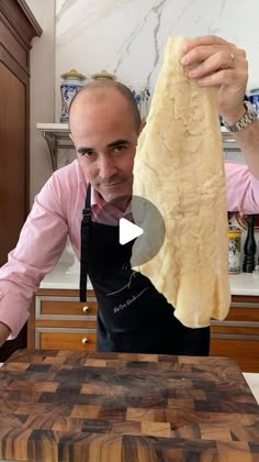 a man in an apron is holding up a piece of bread on a cutting board