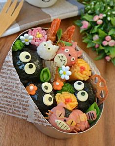 a tin filled with lots of food on top of a wooden table next to flowers