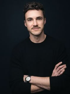 a man with his arms crossed posing for a photo in front of a black background