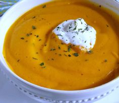 a white bowl filled with carrot soup topped with sour cream and parsley on top