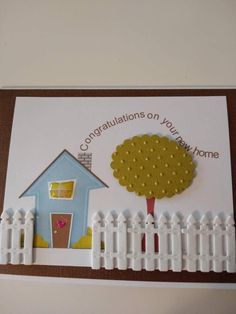 a card with a house and tree on the front, surrounded by white picket fence