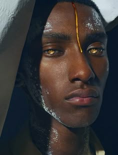 a man with white paint on his face and yellow thread around his eyes, standing in front of a wall