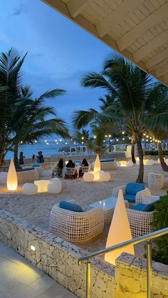 an outdoor seating area with palm trees and lights on the beach in front of it