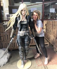 two women standing next to each other in front of cardboard boxes and holding large swords