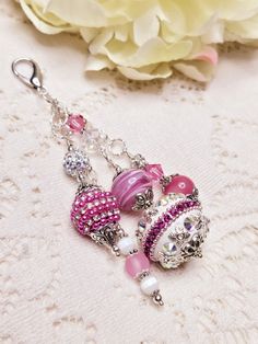 a pair of pink and white beaded earrings on a lace tablecloth with flowers in the background