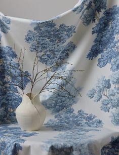 a white vase sitting on top of a table next to a blue and white wallpaper