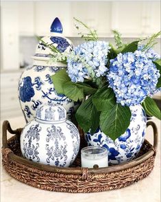 blue and white vases with flowers in them on a wicker tray next to a candle