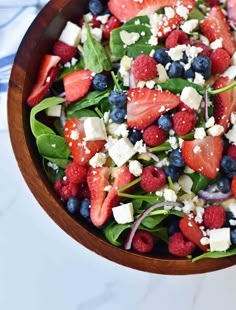 a wooden bowl filled with spinach, strawberries and feta cheese on top