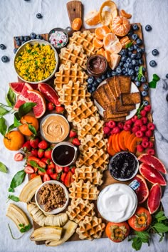 a variety of food is laid out on a white tablecloth with blueberries, strawberries, oranges, and other fruits