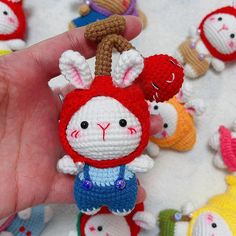 a hand holding a small crocheted keychain in front of many tiny stuffed animals