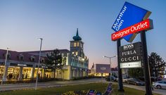 a shopping center with cars parked on the side of the road at dusk, in front of a building that has a clock tower