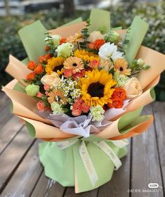 a bouquet of sunflowers and roses wrapped in paper on a wooden table outside