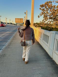 a woman is walking down the sidewalk with her hand in her pocket and purse on her shoulder