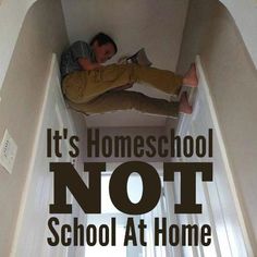 a young boy laying on the floor reading a book with text overlay that reads it's homeschool not school at home