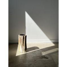 a wooden stump sitting on top of a cement floor next to a white wall and window