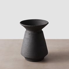 a black vase sitting on top of a table next to a white wall and floor