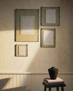 three framed pictures hang on the wall above a small stool in front of a table