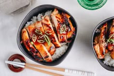 two black bowls filled with meat and rice next to chopsticks on a table