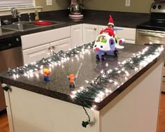 a kitchen island decorated with christmas lights and an elf on the top is surrounded by small toy figurines