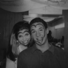 black and white photograph of two people with faces painted like human heads, smiling at the camera