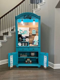 a blue cabinet sitting in the middle of a room next to a stair case with coffee cups on it