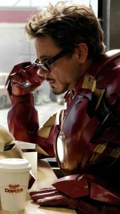 a man dressed as iron man sitting at a table with a cup of coffee in front of him