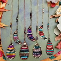 four necklaces with different colors and designs hanging from chains on top of a table