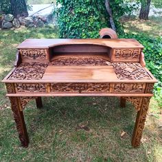 an old wooden desk with carved designs on the top and bottom, sitting in grass