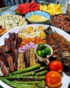 a white plate topped with lots of different types of food next to bowls of vegetables