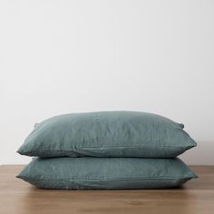 two pillows sitting on top of each other in front of a white wall and wooden floor