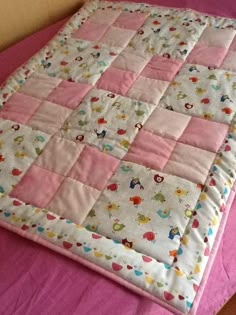 a pink and white quilted blanket on top of a bed