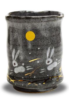 a black and white cup with rabbits painted on the side, in front of a yellow dot