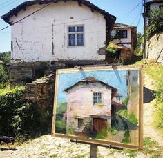 an easel with a painting on it in front of a house and another building