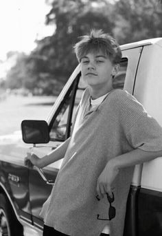 black and white photograph of a boy leaning on the side of a truck with his hand on the door handle