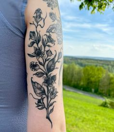 a woman's arm with flowers on it in front of a green field and blue sky