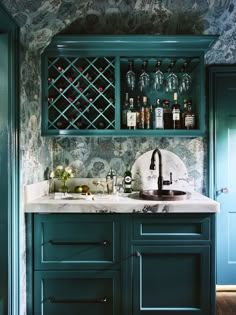 a kitchen with green cabinets and marble counter tops, wine bottles on the shelves above the sink