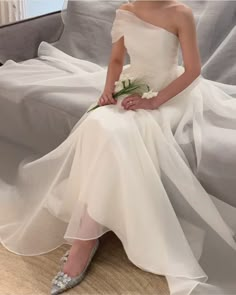 a woman sitting on a couch wearing a white dress and holding a flower in her hand