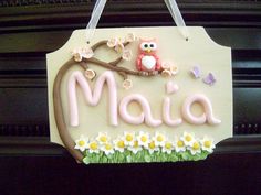 a sign that says maia with an owl sitting on a branch and daisies