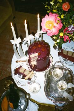 a table topped with cakes and candles on top of a white tablecloth covered in flowers