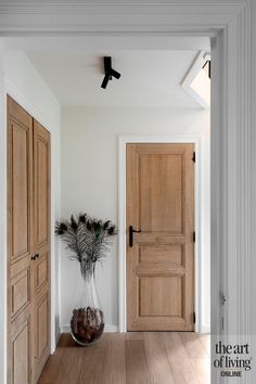 a vase with some plants in it sitting on the floor next to two wooden doors