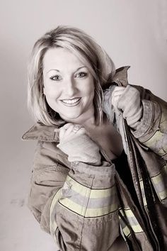 a woman wearing a fireman's jacket and holding onto her coat while posing for the camera