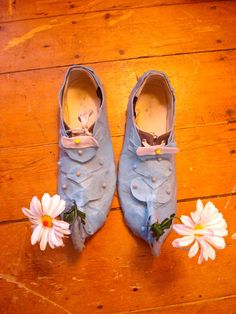 a pair of blue shoes sitting on top of a wooden floor next to white flowers