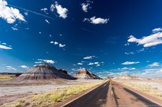 an empty road in the desert under a blue sky with white clouds and some hills