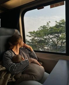 a woman sitting on a train looking out the window with her baby in her lap