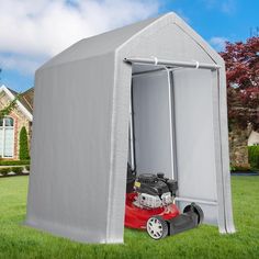 a red lawn mower sitting inside of a large gray shed on top of green grass