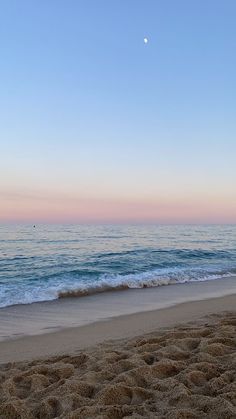 a beach with waves coming in to shore and the moon rising over the ocean on a clear day