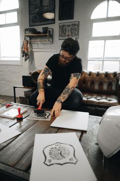 a man sitting at a table working on some art work with scissors and paper in front of him