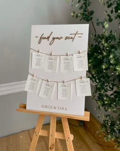 a sign with seating cards attached to it on a wooden easel next to a potted plant