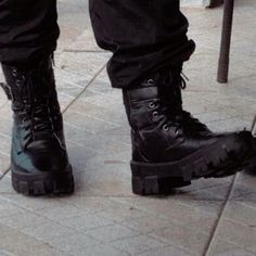 a person wearing black boots standing on a sidewalk