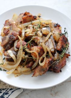 a white plate topped with meat and onions on top of a marble countertop next to a napkin